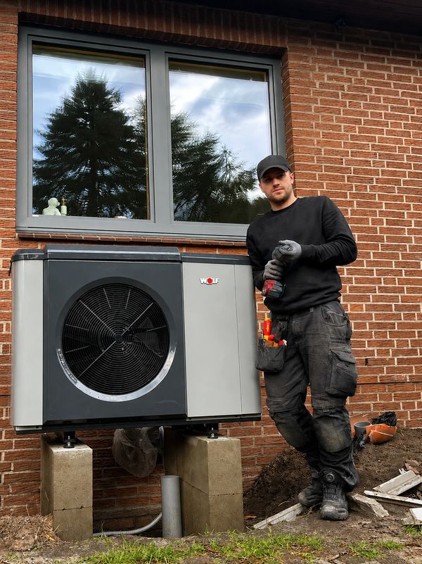 Mann neben installierter Wärmepumpe vor einem Backsteinhaus.