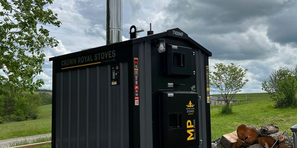 Black outdoor wood stove with chimney in a rural setting.