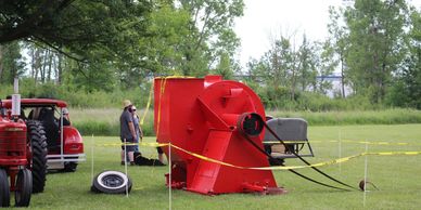 A large red agricultural machine on grass near a tractor.