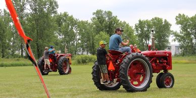 Two people riding vintage red tractors on a grassy field.