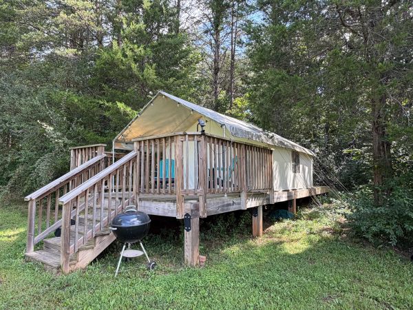 Wooden deck with tent and grill in forest clearing.