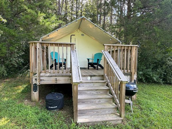 Raised tent cabin with turquoise chairs and grill.