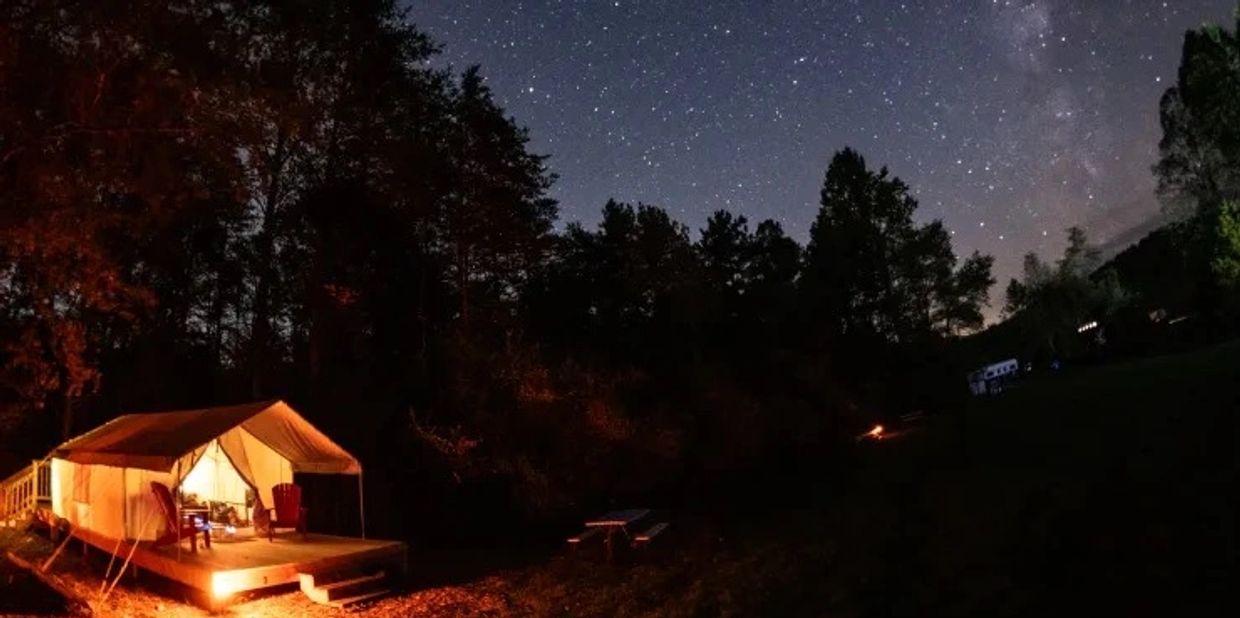 Lit tent under a starry night sky near trees.