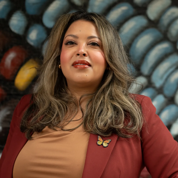 Confident woman with long hair wearing a red blazer and butterfly pin.