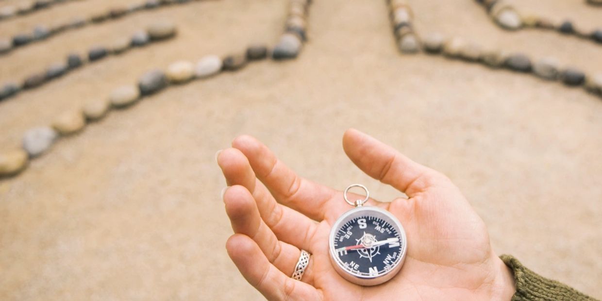 Hand holding a compass with stone patterns in the background.