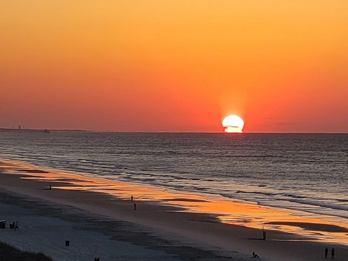 Sunset over a calm ocean with a sandy beach reflecting orange hues.