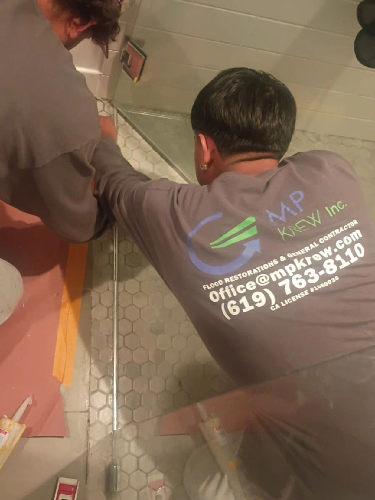 Two workers repairing hexagonal floor tiles by a bathtub.