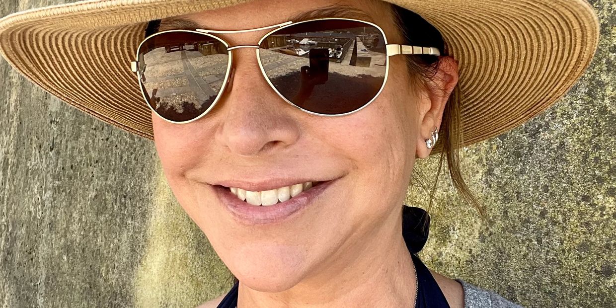 Woman wearing a sunhat and reflective sunglasses, smiling outdoors.