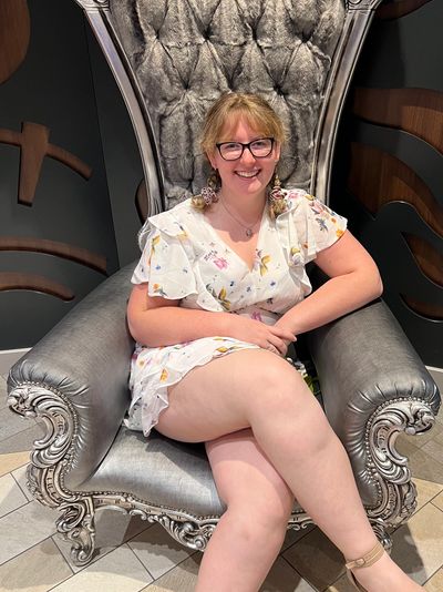 Smiling woman in floral dress sits on an ornate silver chair.