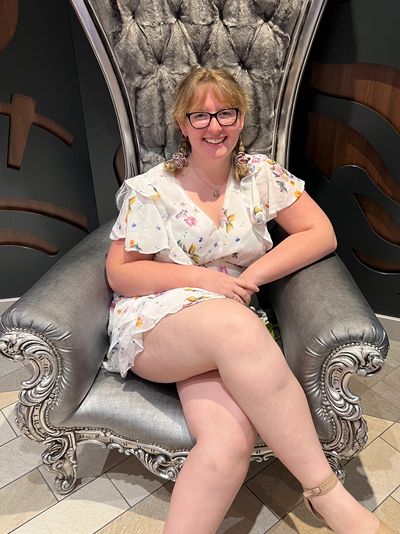 Smiling woman in floral dress sits on an ornate silver chair.