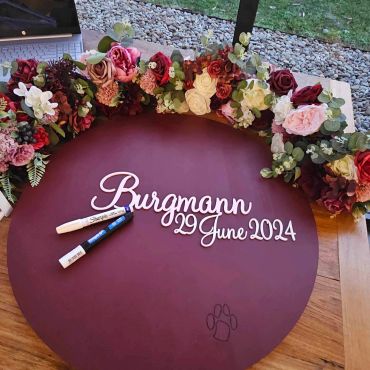 Floral wreath surrounding burgundy board for 29 June 2024.