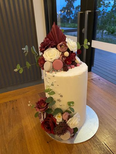 Elegant white cake decorated with flowers and macarons.