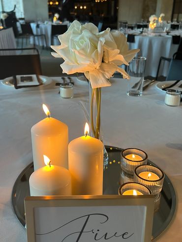 Elegant table centerpiece with white candles and a white rose.