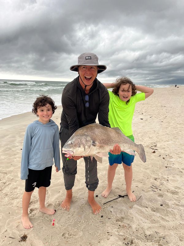 Family joy on a beach with a big fish catch under cloudy skies.