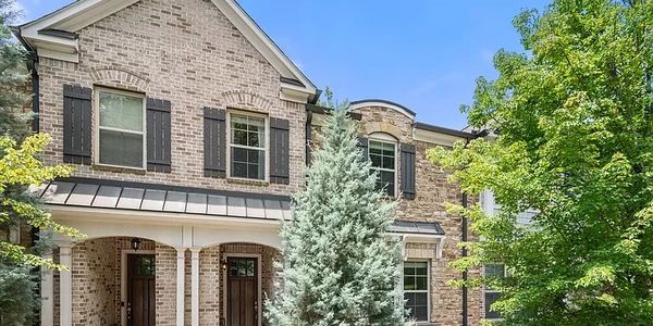 Two-story brick townhouses with greenery and blue sky.