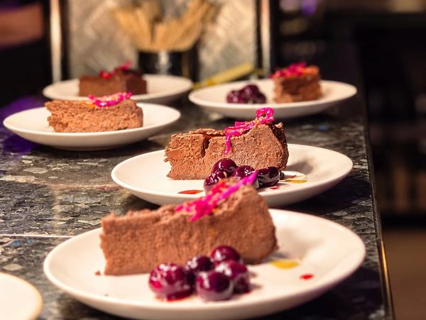 Chocolate mousse cake slices with cherries on white plates.