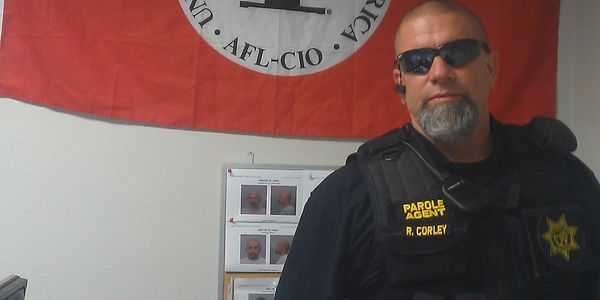 Parole agent in tactical gear stands indoors with a union flag behind him.