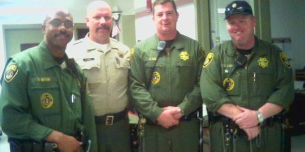 Four uniformed law enforcement officers posing indoors, smiling.