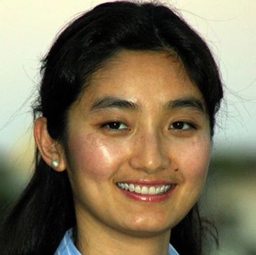 A smiling woman with dark hair and pearl earrings.