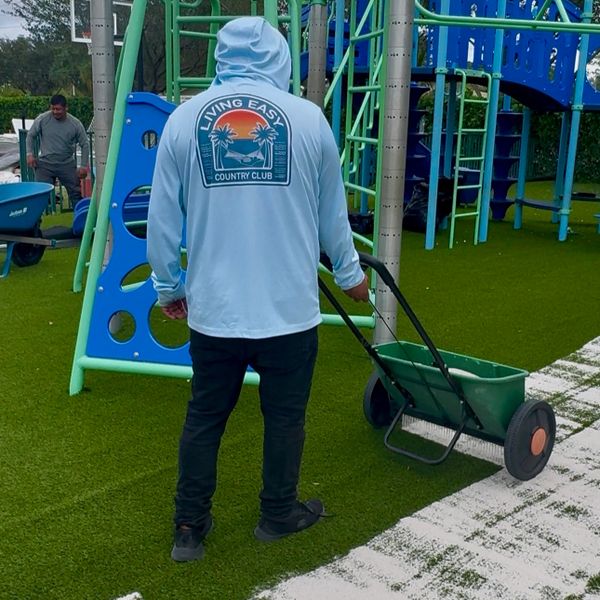 Person in light blue hoodie working on playground turf with a spreader.