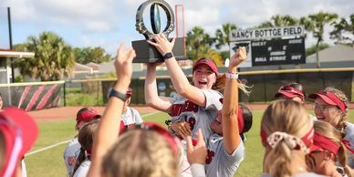 Team celebrates holding up a trophy on a softball field.