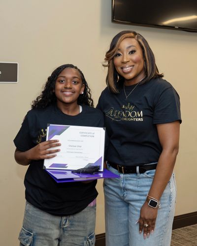 Two smiling females holding a certificate and wearing matching black t-shirts.