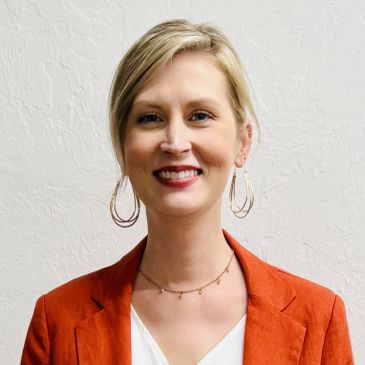 Smiling woman in an orange blazer and large hoop earrings.