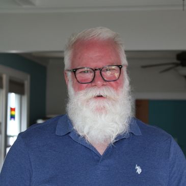 Elderly man with white beard and glasses smiling.