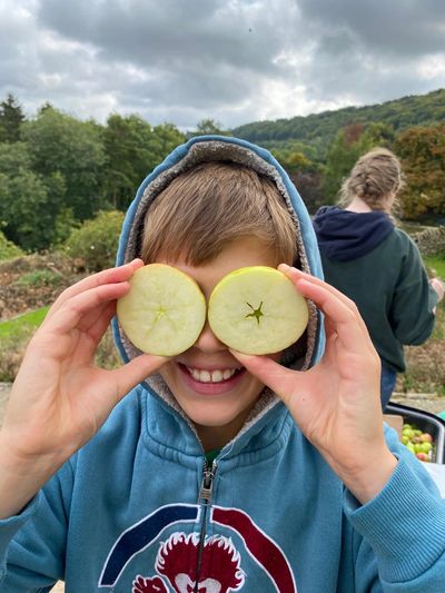 Child holding apple slices over eyes, smiling outdoors.