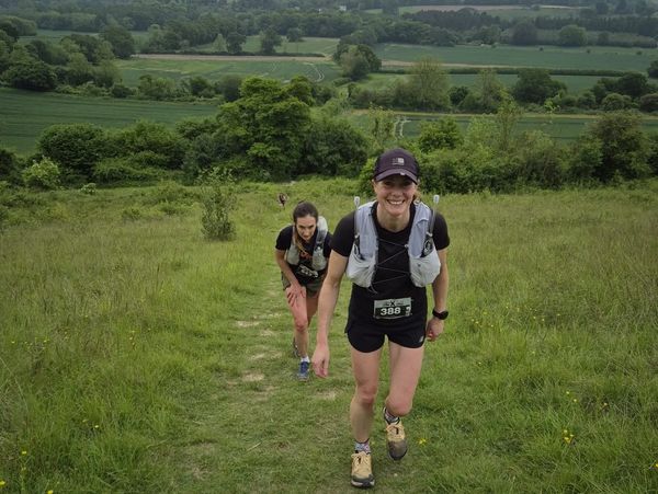 Two women hiking uphill in a lush green landscape, one smiling at the camera.