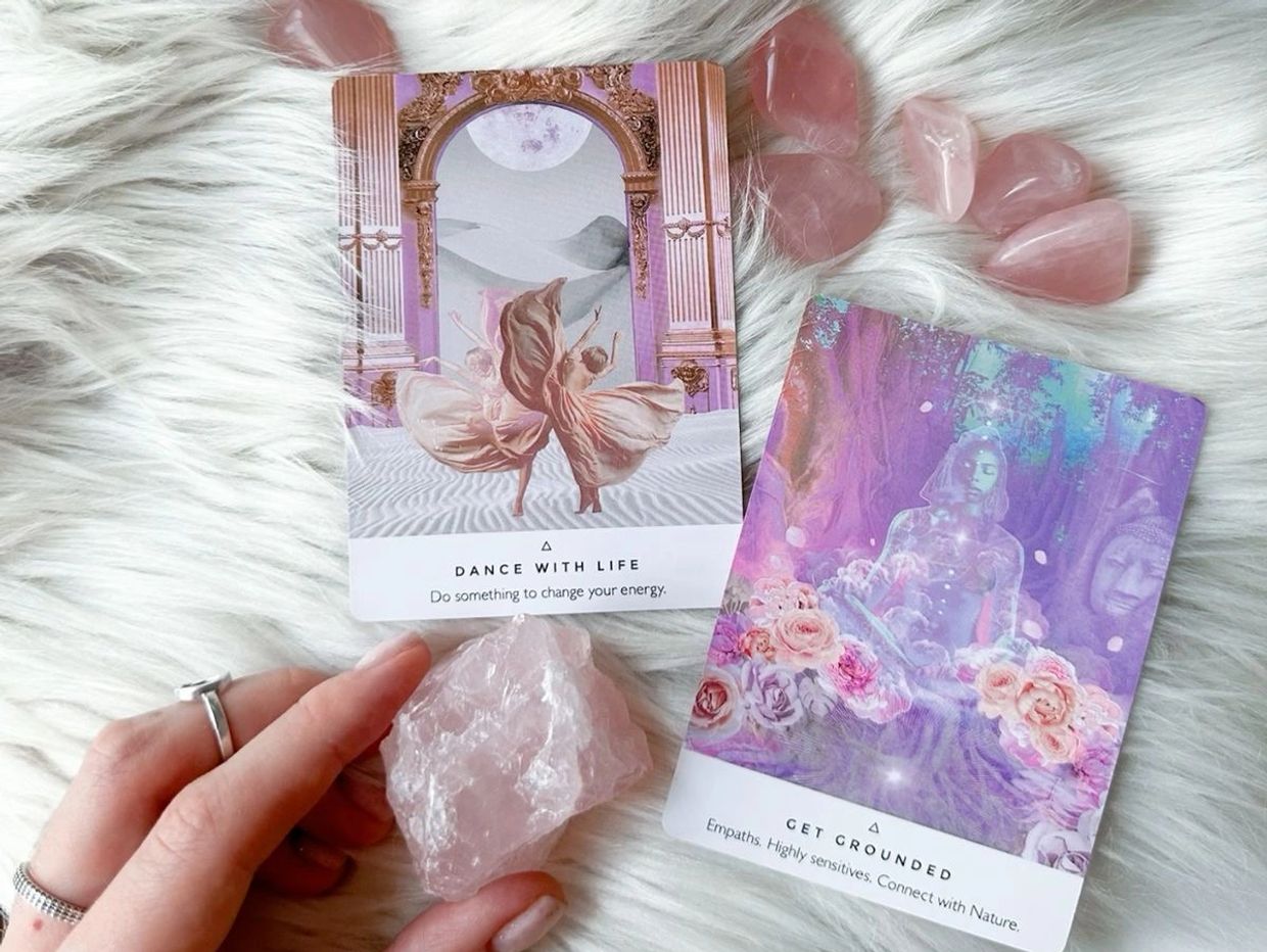 Two spiritual oracle cards with rose quartz crystals on white fur.