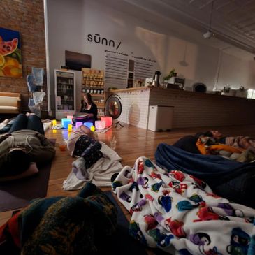 People lying on the floor in a cozy, dimly lit room with colorful blankets and soft lighting.