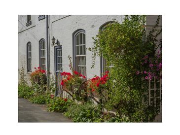 White building with arched windows and colorful flowers along the wall.