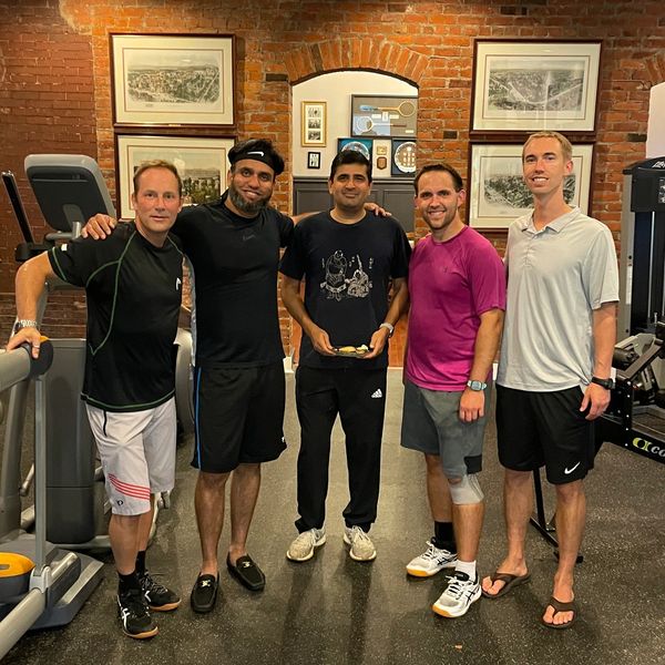 Five men posing together in a gym with exercise machines.
