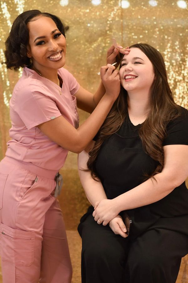 A beautician shapes a client's eyebrows with a smile.