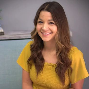 A smiling woman with long wavy hair in a yellow top.