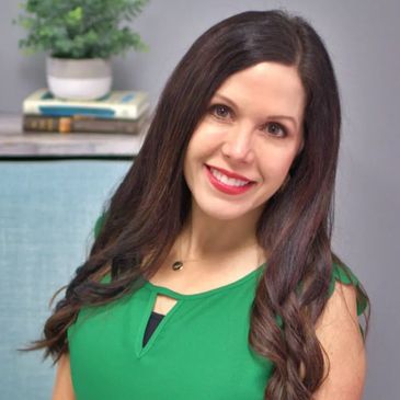 Smiling woman with long dark hair in a green top sitting on a blue chair.