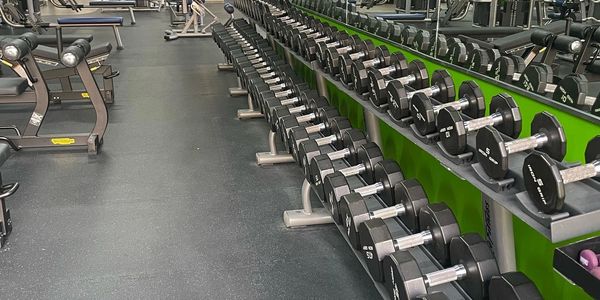 Well-equipped gym with rows of dumbbells and workout machines.