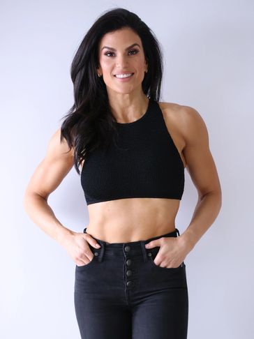 Fit woman in black crop top and high-waisted jeans smiling at the camera.