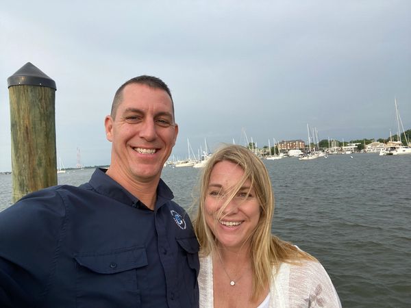 Smiling couple by the waterfront with boats in the background.