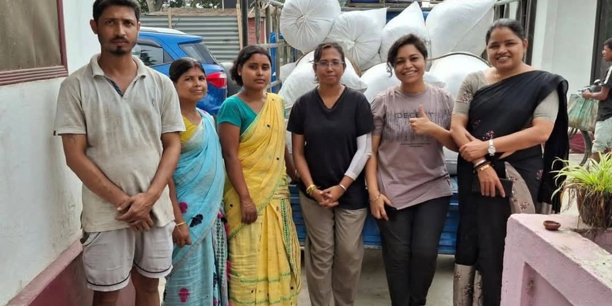 A group of six people standing outdoors with bags in the background.
