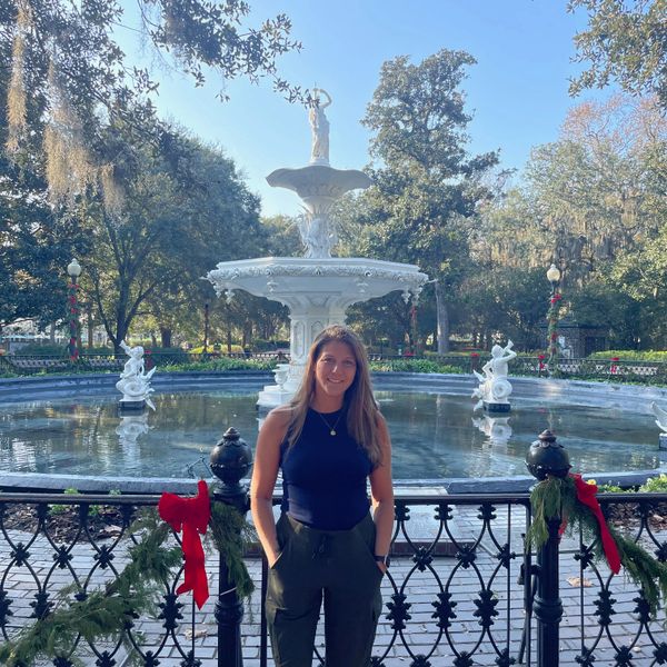 Woman posing in front of a decorated fountain in a park on a sunny day.
