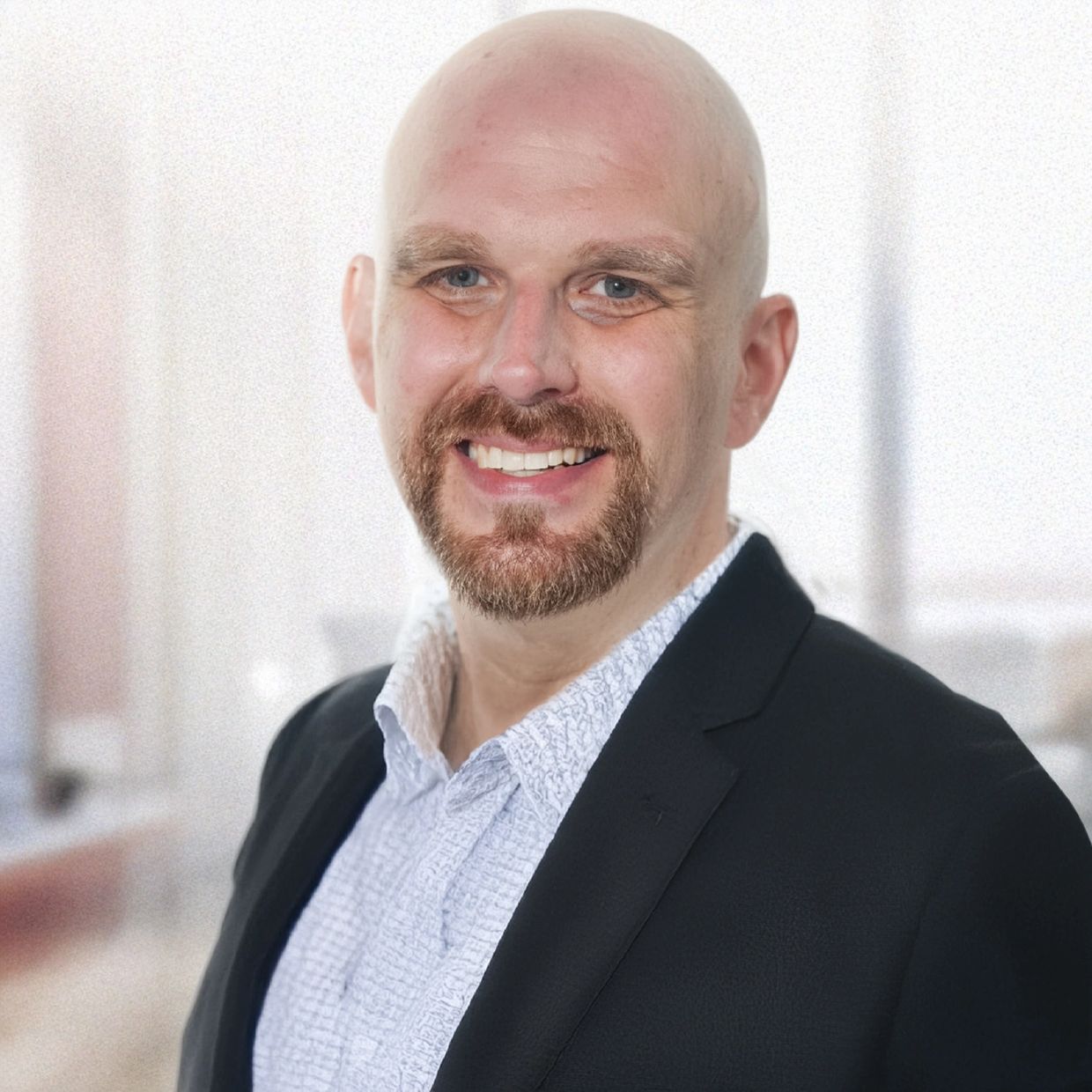 Smiling bald man with a beard in a black blazer and patterned shirt.