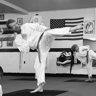 Two martial artists practicing kicks indoors.