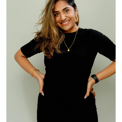 Smiling woman in black dress posing with hands on hips.