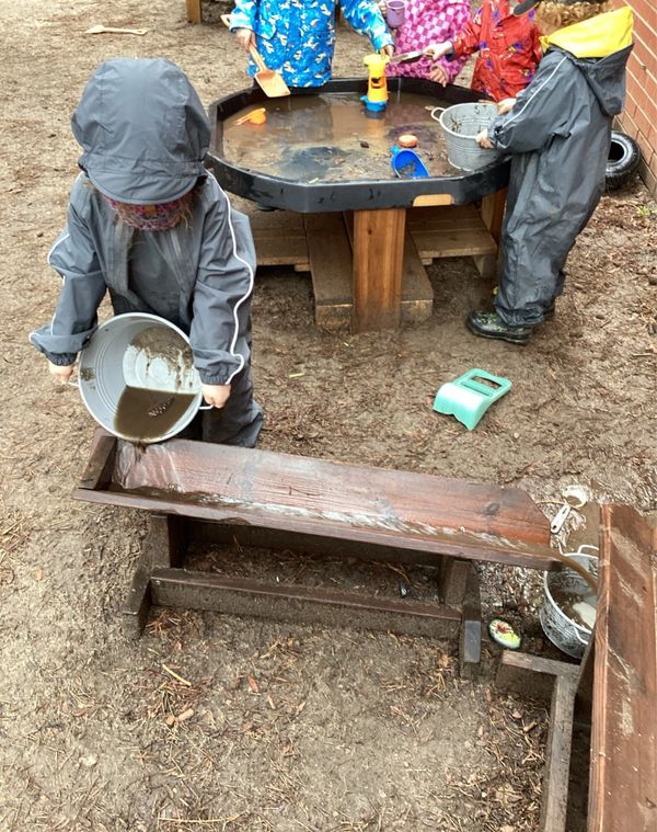 Children in rain suits play with water and mud outdoors.