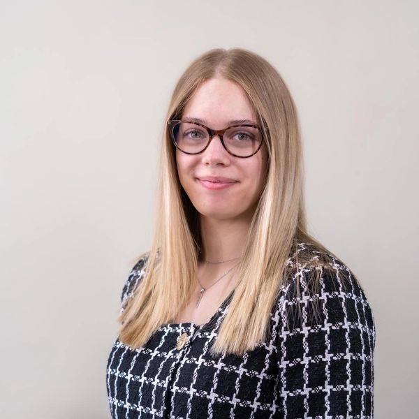 Young woman with glasses smiling against a plain background.