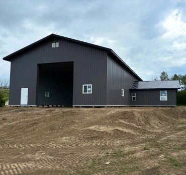 Newly constructed large dark gray metal barn on cleared land.