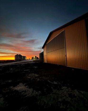 Sunset over a farm with large barns and silos.