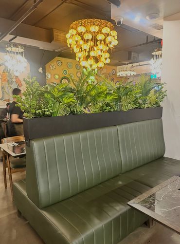 Green leather booth seating with plants and golden chandeliers in a stylish restaurant.